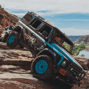 Custom off-road SUV climbing rocky terrain near a canyon with scenic river in background