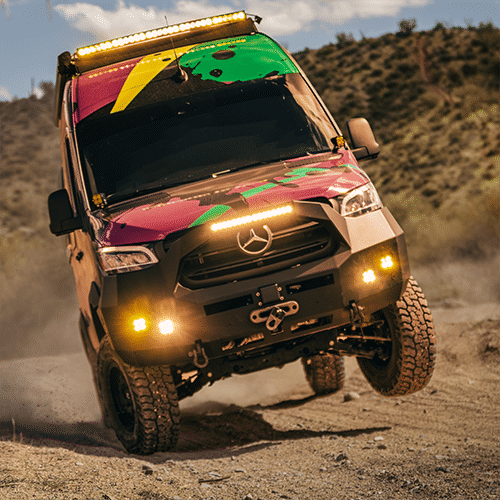 Off-road Mercedes camper van with colorful wrap kicking up dust on rugged terrain
