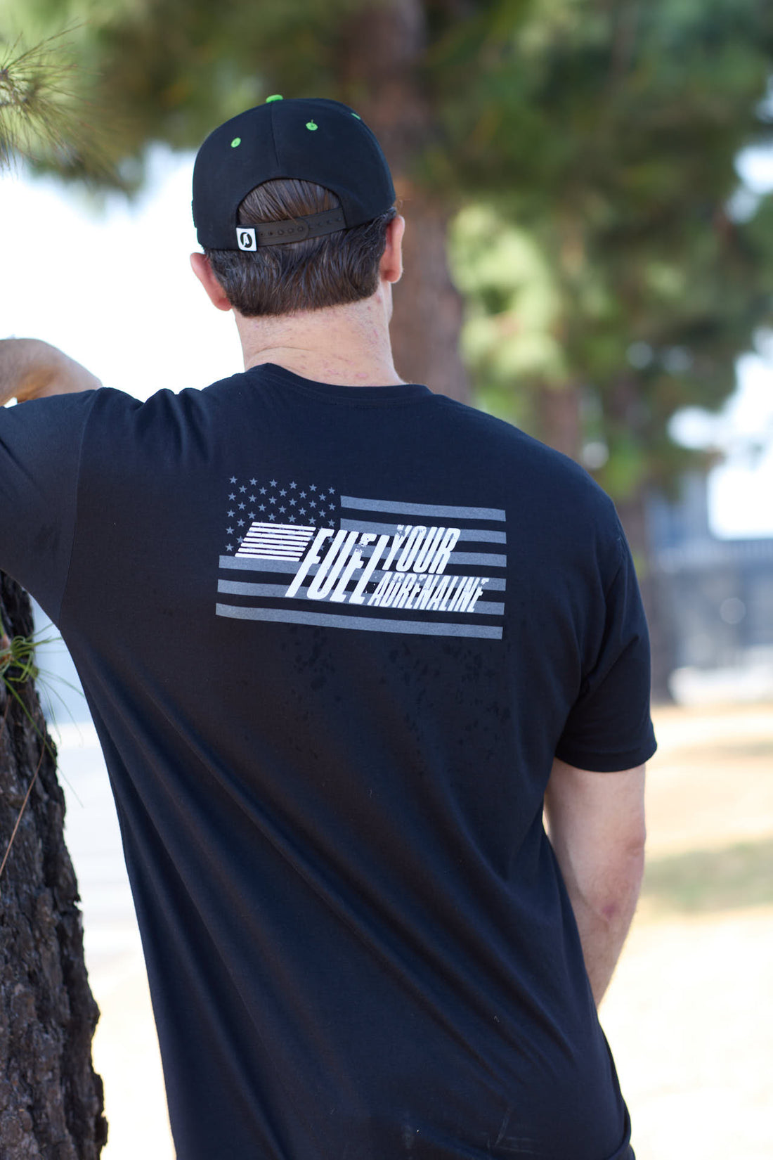 Man outdoors wearing black tee with American flag and 'Fuel Your Greatness' on the back