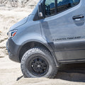 Close-up of off-road van tire on sandy terrain with rugged tread pattern.