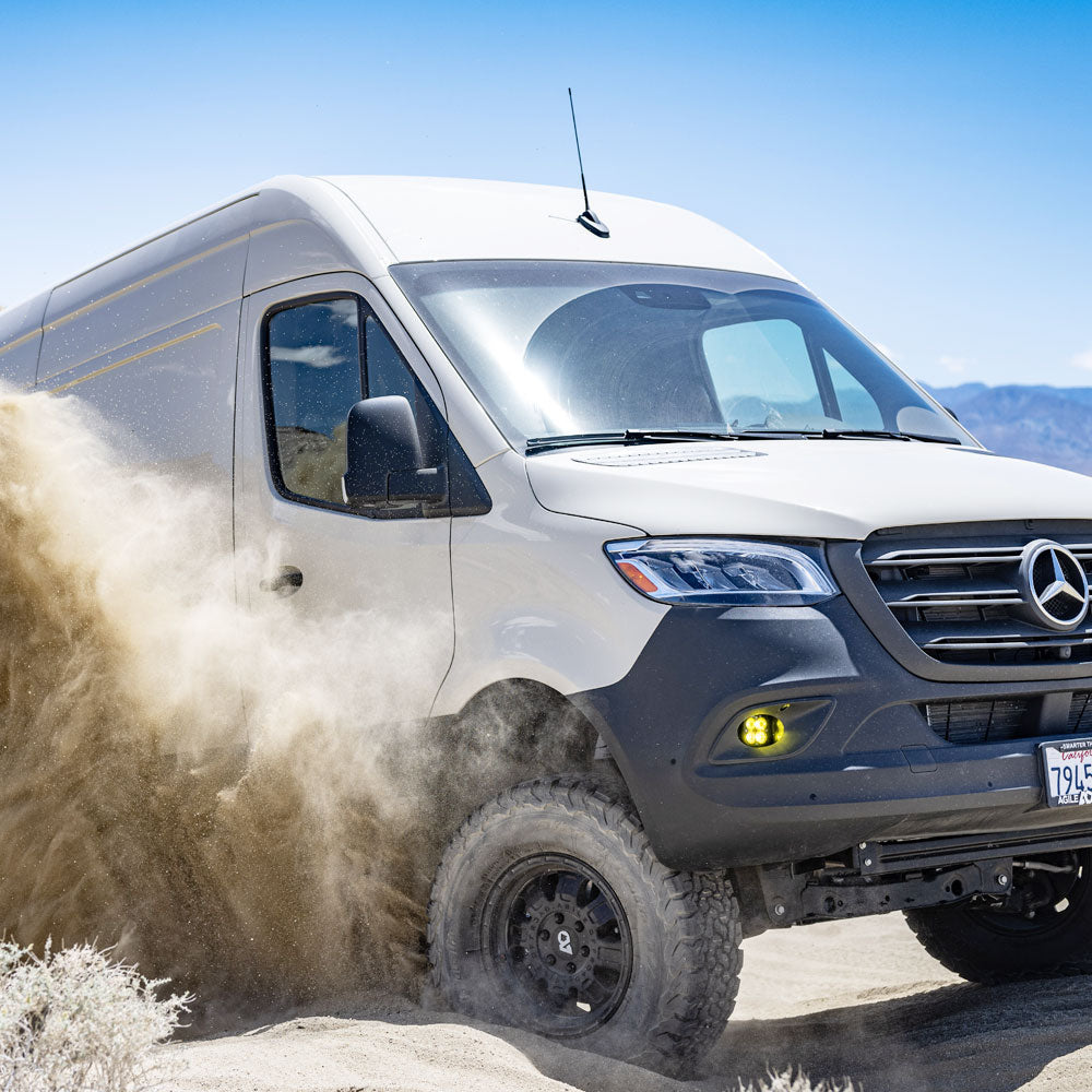 Off-road Mercedes-Benz Sprinter van driving through desert sand with dust flying