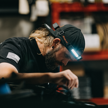 Man wearing a lighted headlamp, focused while working in a workshop.