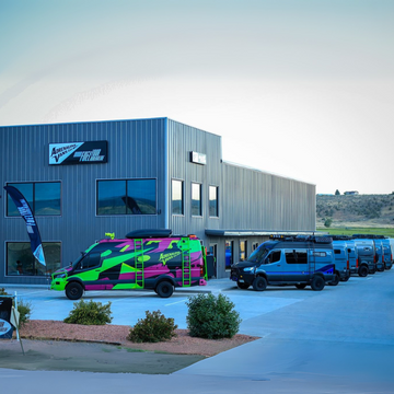 A row of custom off-road vans parked outside a modern industrial building.