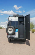 Rear view of an off-road camper van with rear doors open and a mounted spare tire.