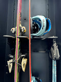 Close-up of two snowboards with bindings, vertically stored on a black rack.