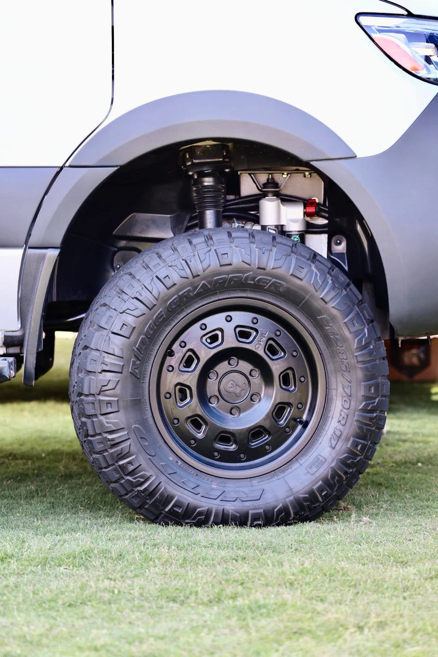 Close-up of a rugged off-road tire and suspension system on a parked truck.
