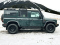 Green off-road SUV parked on snowy mountain terrain with pine trees in background