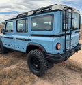 Light blue off-road SUV with black ladder and rugged tires parked on a dirt trail.
