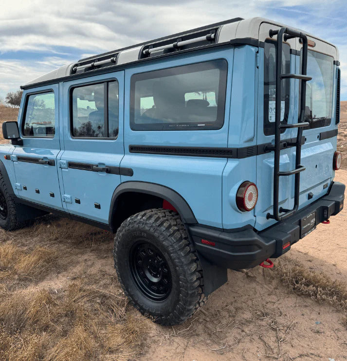 Light blue off-road SUV with black ladder and rugged tires parked on a dirt trail.