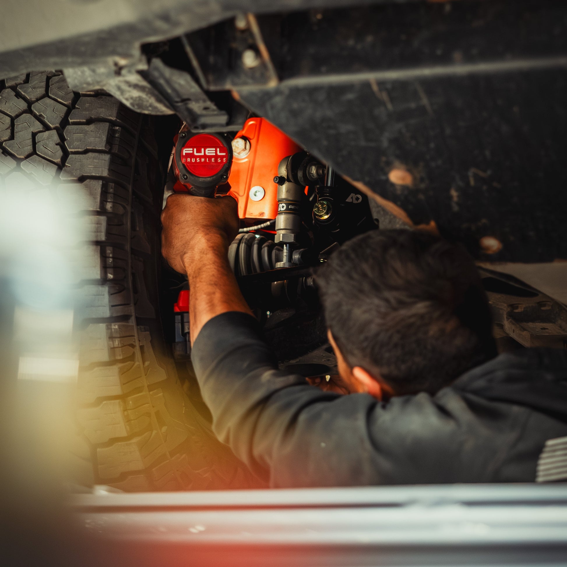 Mechanic installs red FUEL suspension component under off-road vehicle