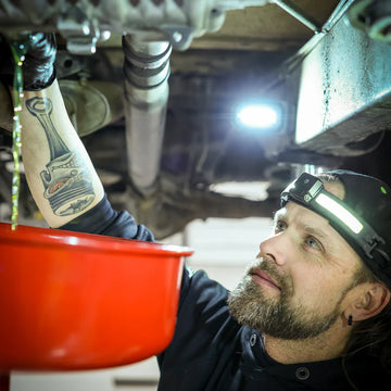 Man wearing headlamp draining oil from car engine into red container