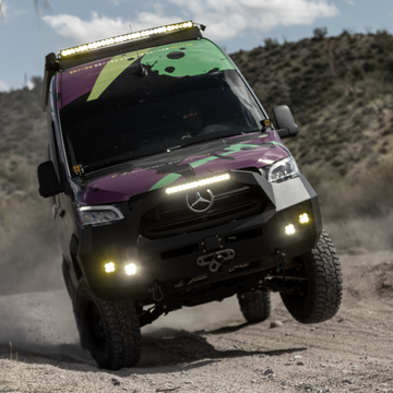 Lifted Mercedes-Benz Sprinter van with off-road lights and camo wrap driving on a dirt trail