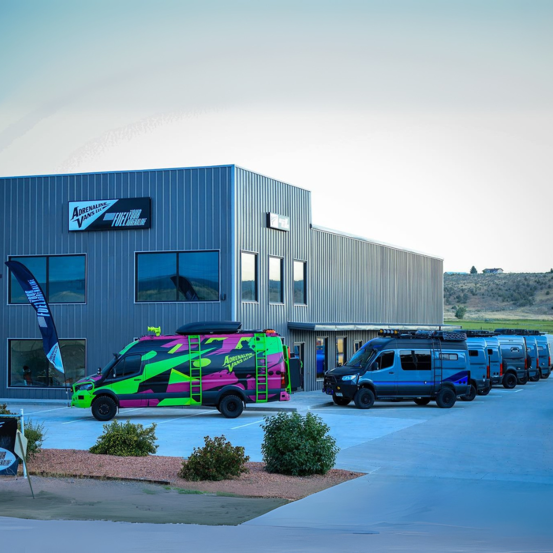 A row of custom off-road vans parked outside a modern industrial building.