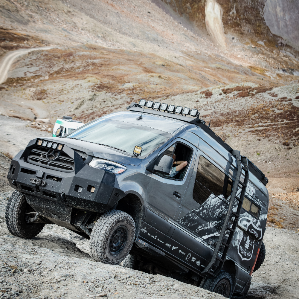 Lifted off-road van with rugged tires and mountain graphics climbing a rocky hill trail.